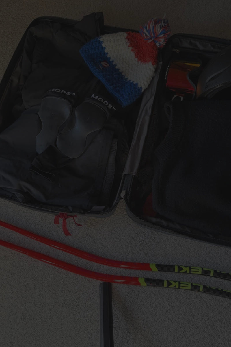 MODS shin protection sleeves with raised gel padding packed with ski clothing, a winter hat and ski poles, designed to help reduce shin pressure and discomfort inside ski boots.