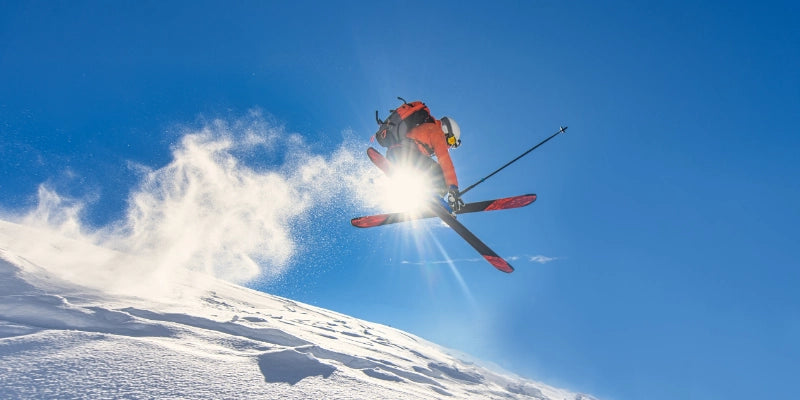 Skier performing an aerial jump above a snowy mountain slope beneath a clear blue sky.