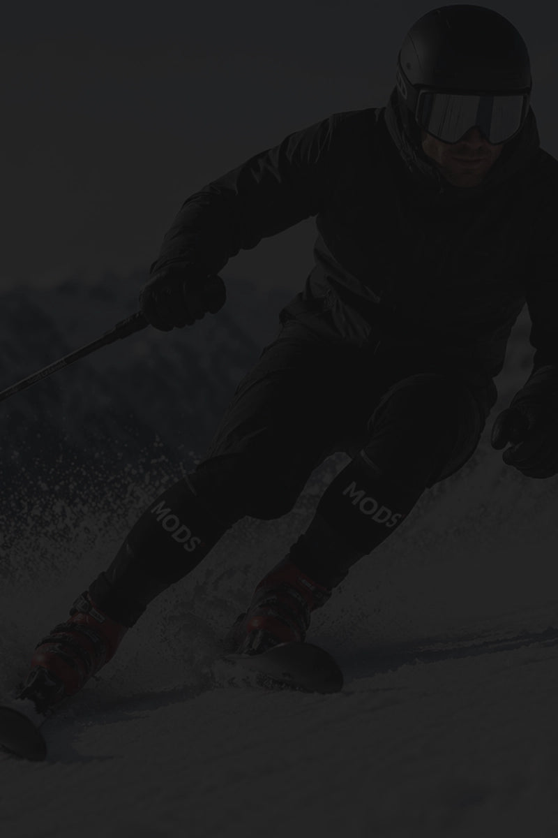 Skier carving through snow while wearing the MODS ski support system on both lower legs.