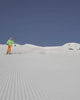 Skier in green and orange clothing descending a freshly groomed snow-covered slope.